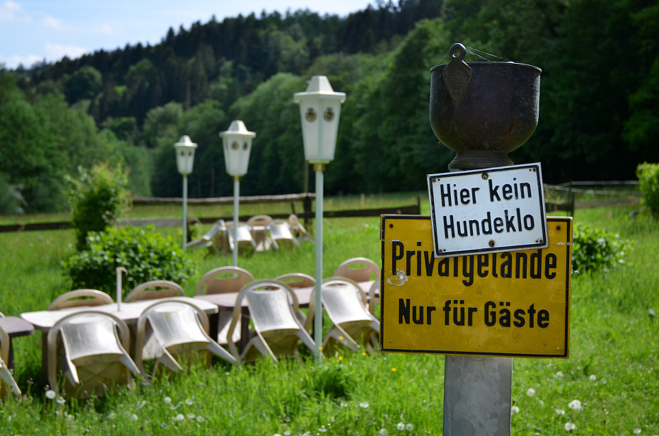 Biergarten mit zwei Schildern, die den Text 'Hier kein Hundeklo' und 'Privatgelände - Nur für Gäste' tragen.