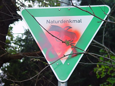 Grnes Hinweisschild mir der Aufschrift Naturdenkmal. Ein Sprayer legte roten Font an. Gesichtet in Birkendahl-Aufderhhe-Solingen